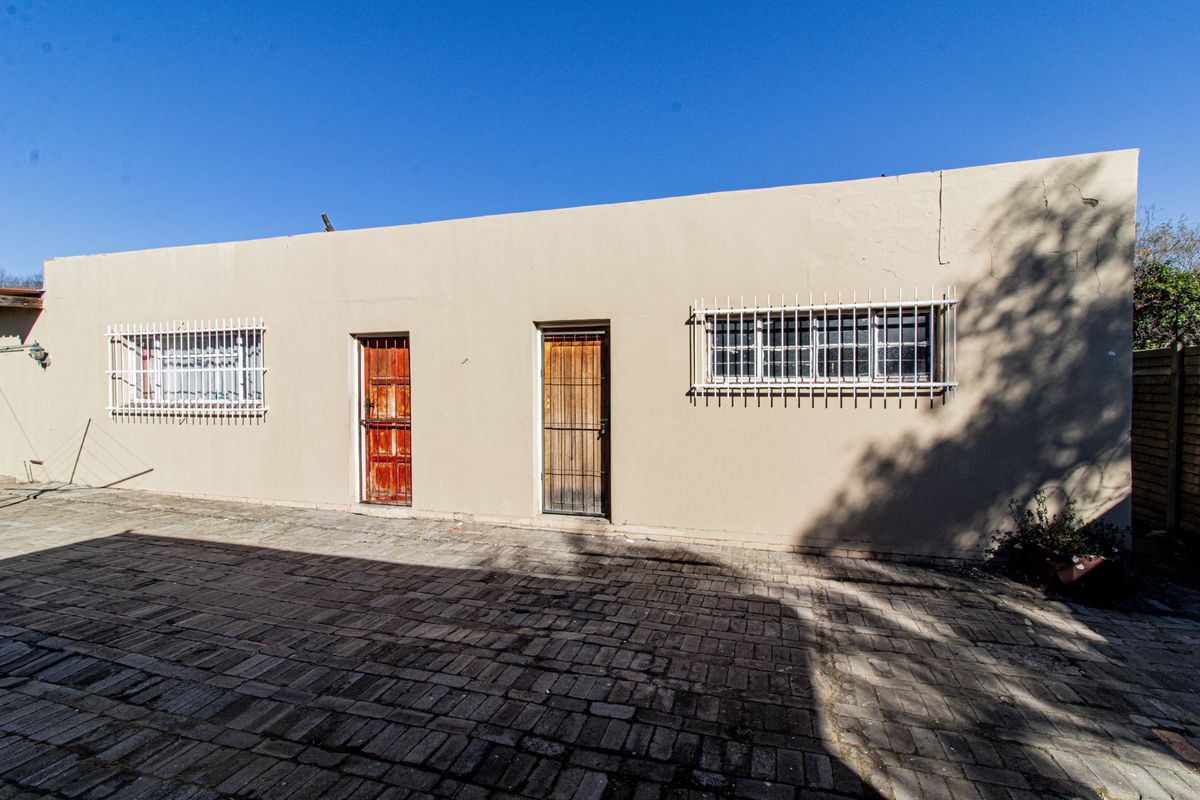 Rear exterior view of the property featuring a paved courtyard, security bars on windows, and two timber entrance doors.
