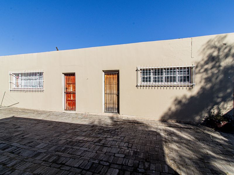 Rear exterior view of the property featuring a paved courtyard, security bars on windows, and two timber entrance doors.
