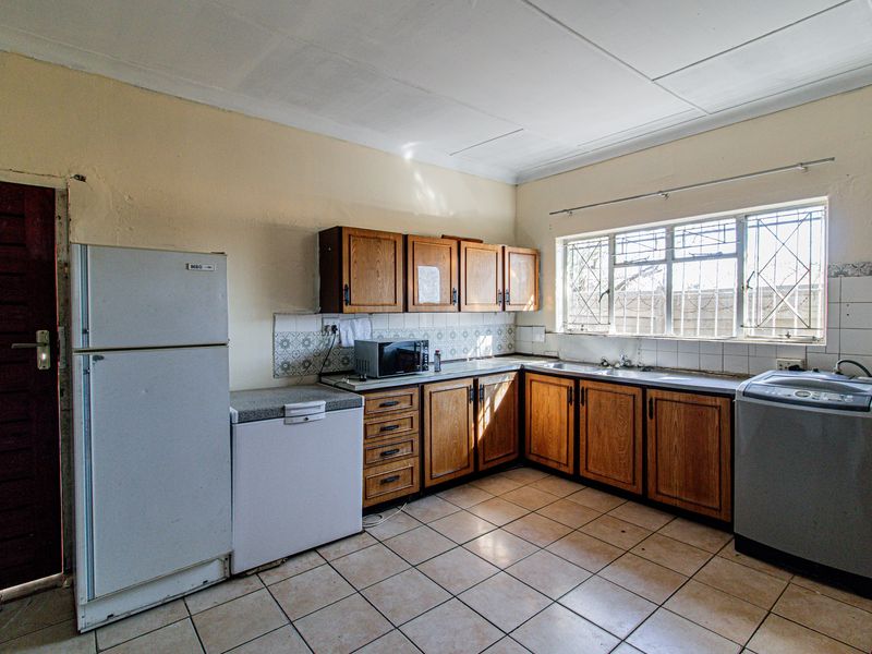 A functional kitchen featuring wooden cabinetry, tiled flooring, and a tiled backsplash, offering a dated aesthetic with potential for modernization.
