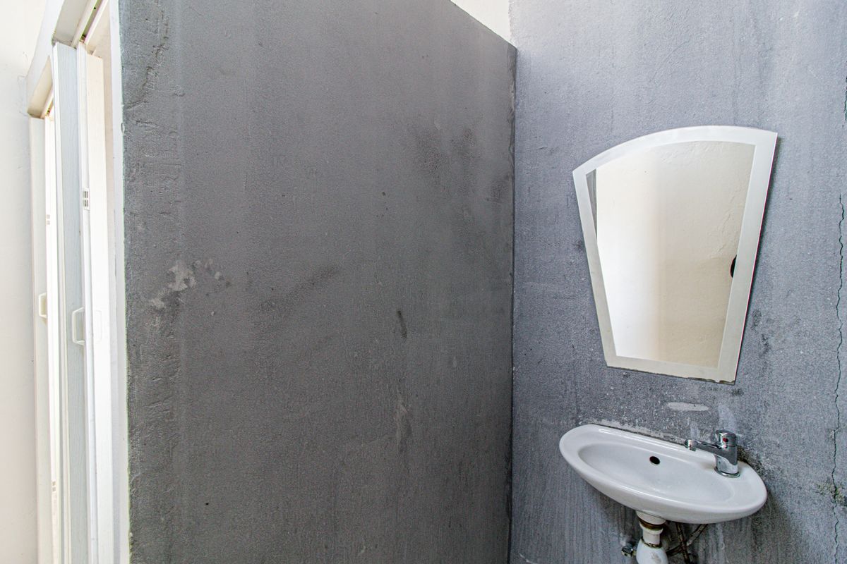 A small bathroom featuring a wall-mounted basin with a chrome mixer tap and a wall mirror, currently requiring wall finishing and repairs.