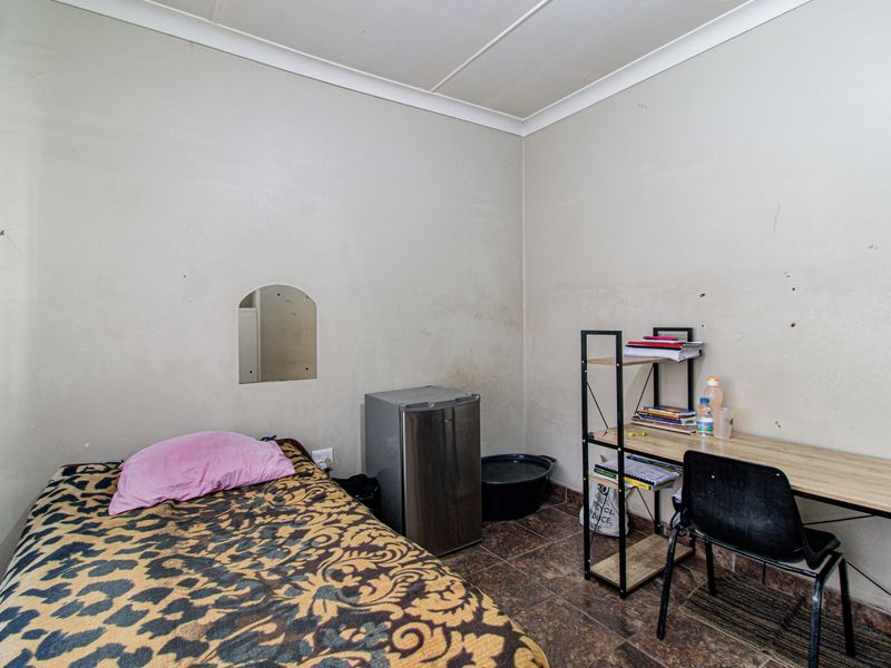 A compact bedroom featuring tiled flooring and neutral walls, currently utilized as a functional living space.