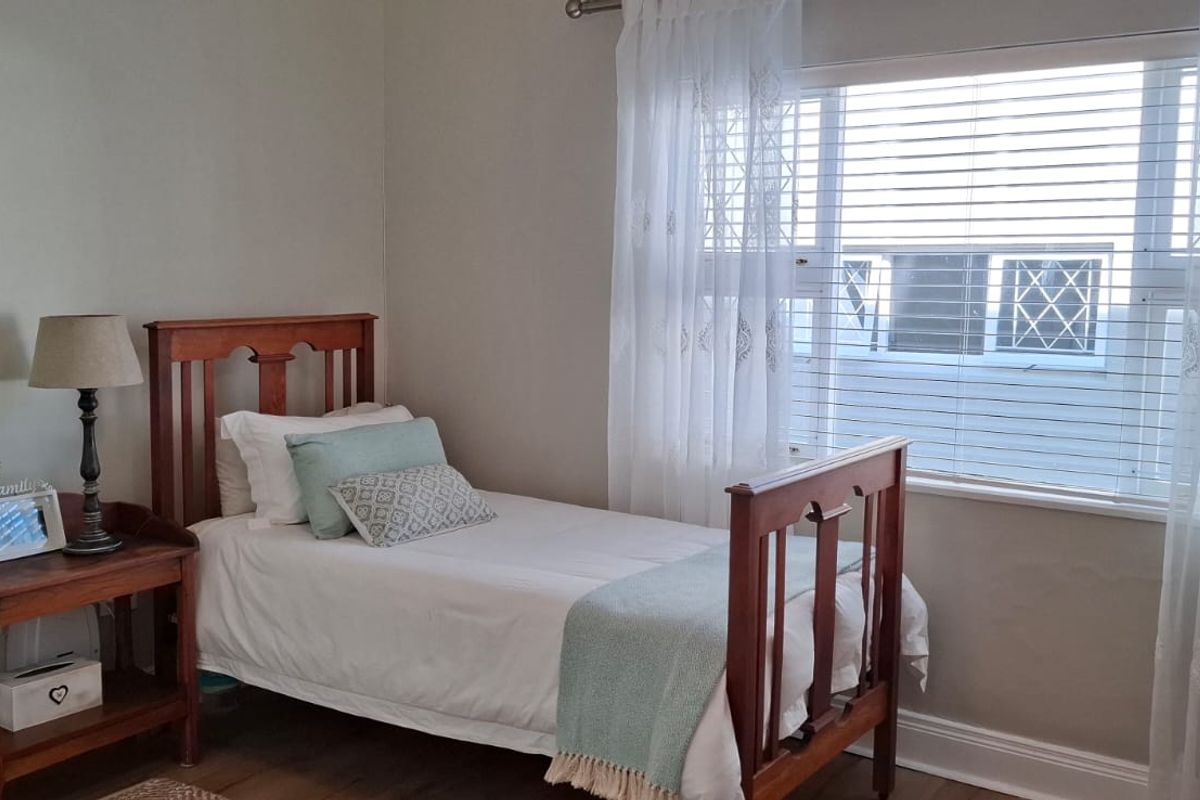 A well-lit bedroom featuring neutral walls, timber-look flooring, and a large window with fitted blinds and curtains.