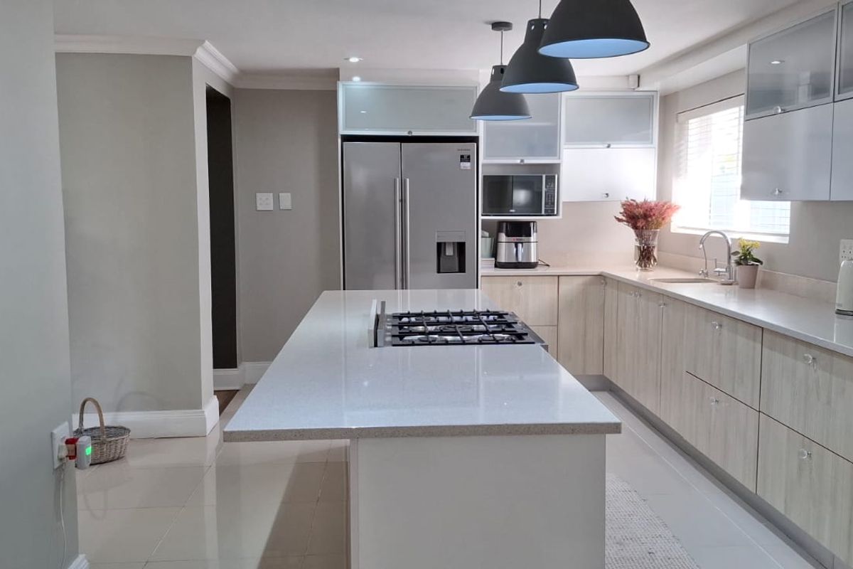 Modern kitchen featuring a central island with a built-in gas hob, light wood cabinetry, stone countertops, and contemporary pendant lighting.