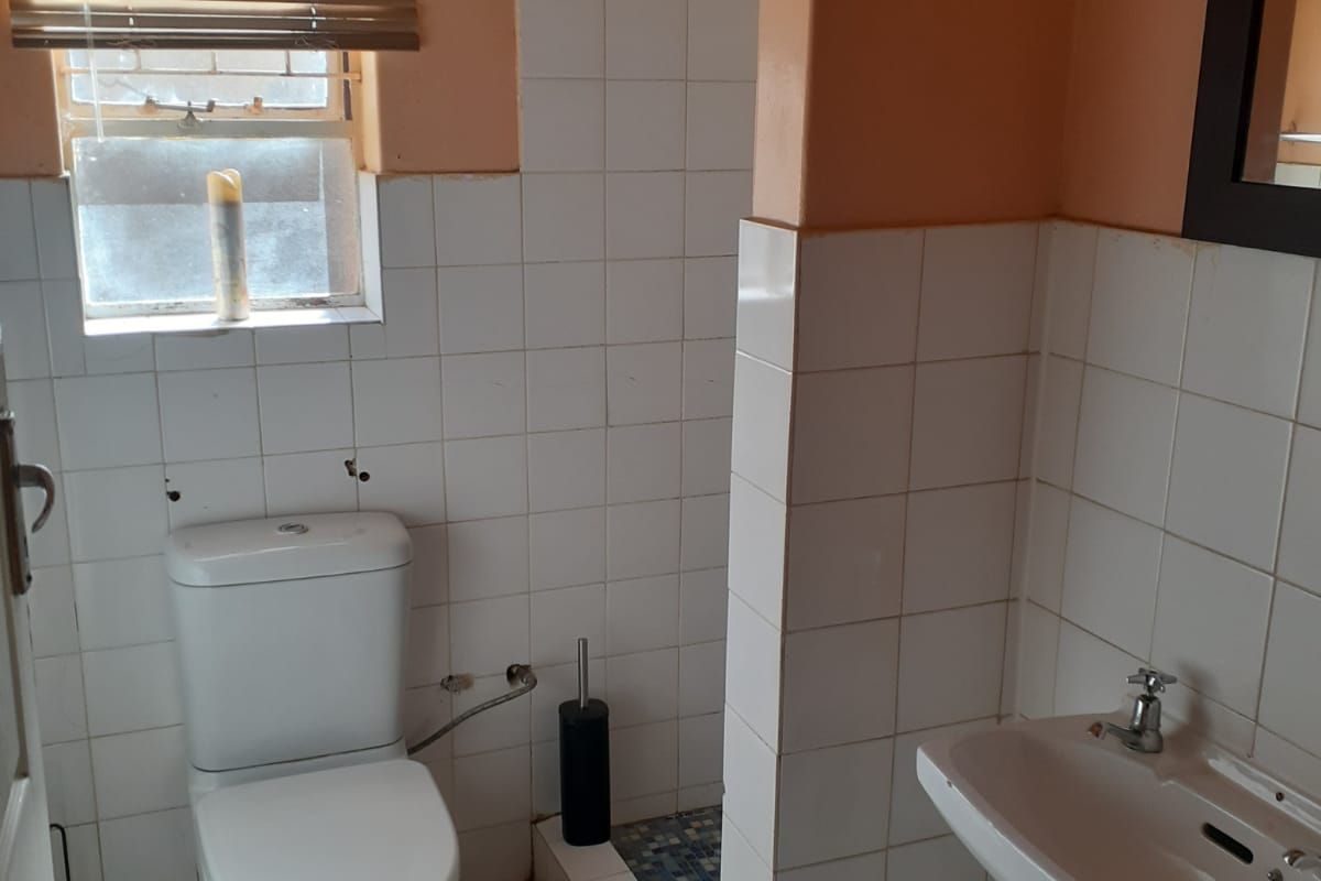 A functional bathroom featuring a standard toilet, wall-mounted basin, and tiled shower area with a window for natural light.