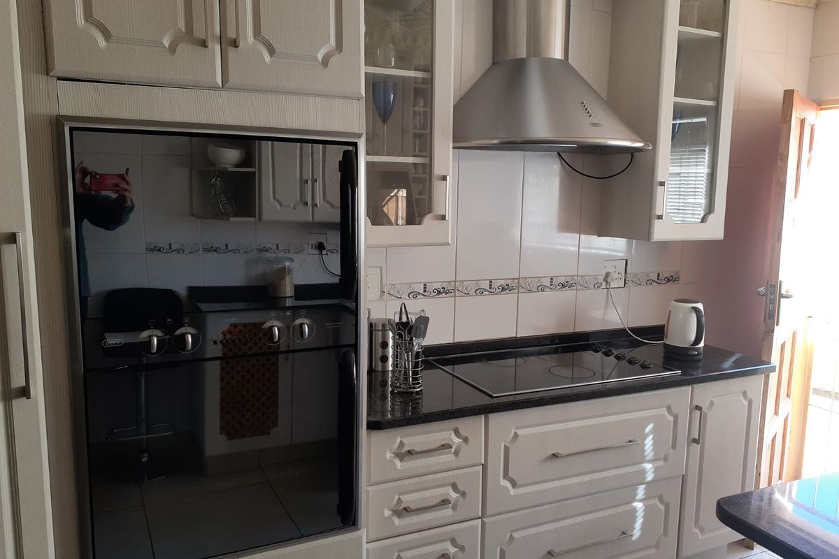 A functional kitchen featuring built-in cabinetry, a dark granite countertop, a glass-top hob, a stainless steel extractor fan, and a built-in oven.
