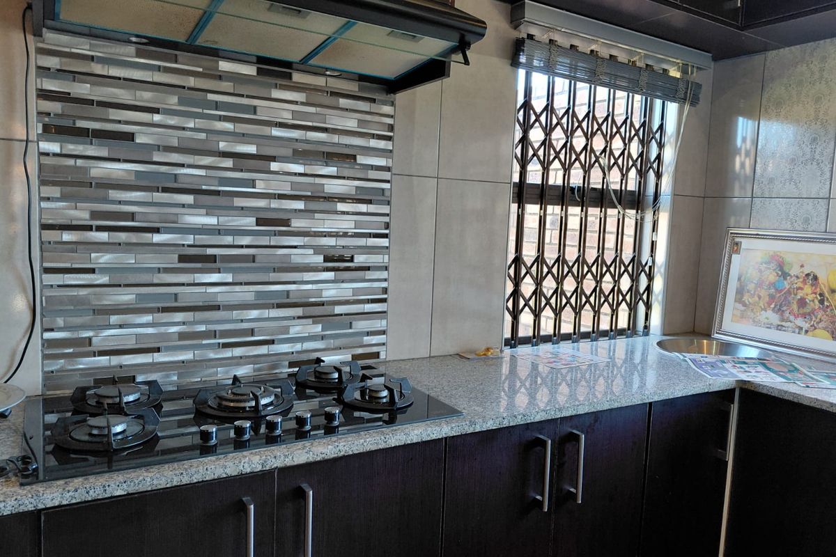 Modern kitchen featuring dark cabinetry, granite countertops, a gas hob with extractor fan, and a decorative tiled backsplash.