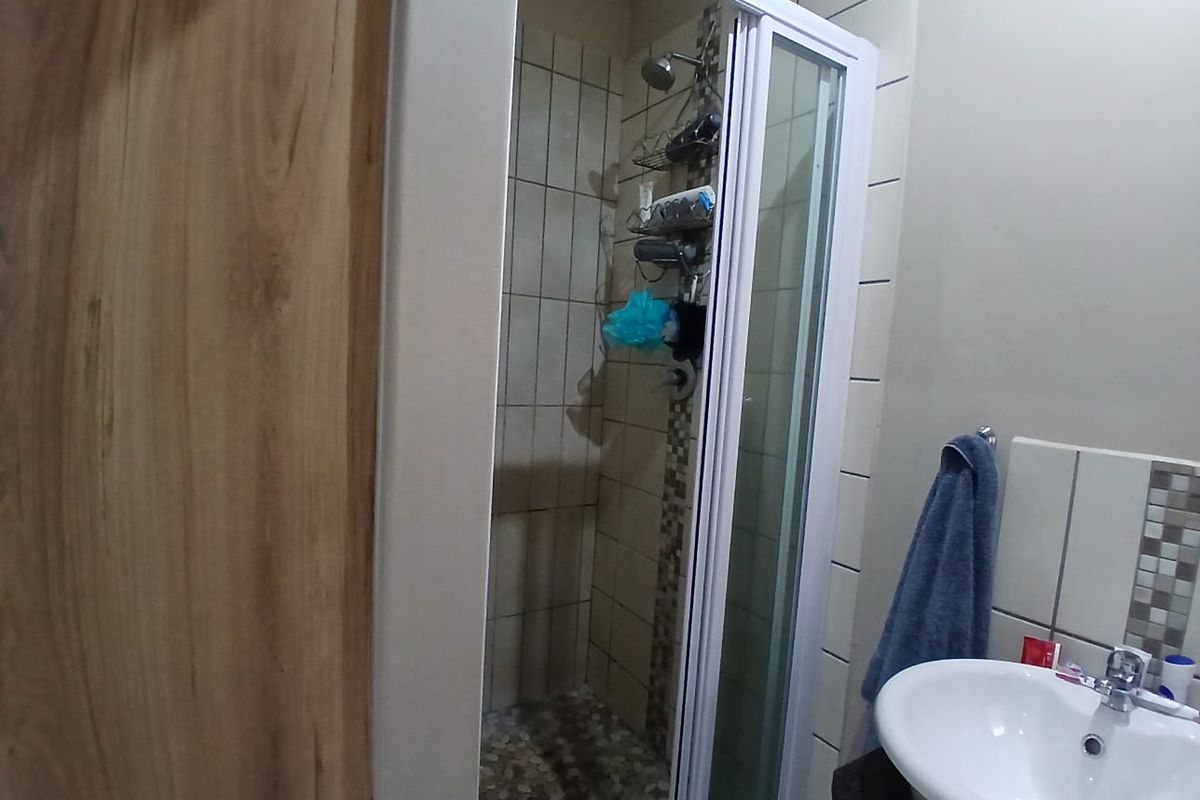 A functional bathroom featuring a shower enclosure with pebble tile flooring, a pedestal basin with a modern mixer tap, and neutral wall tiling.