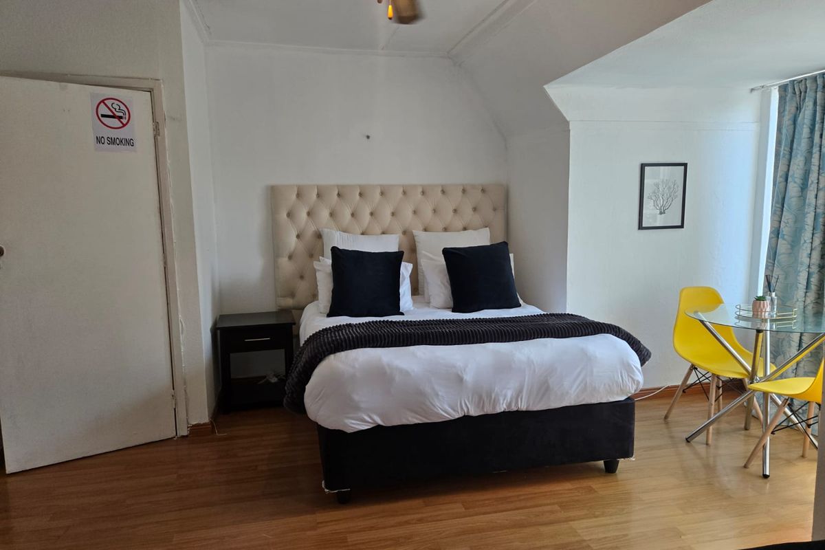 A bedroom featuring laminate flooring and a ceiling fan, with a neutral color palette and sloped ceiling detail.