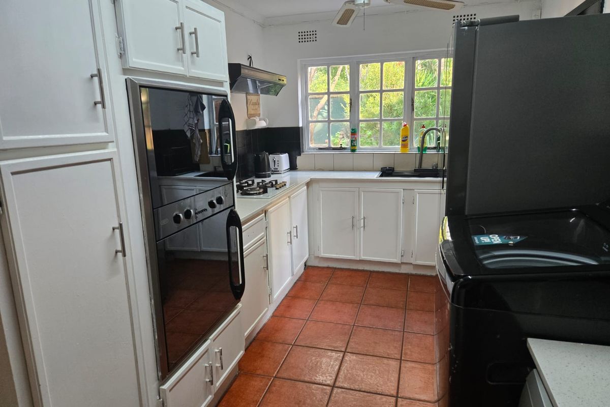 Functional kitchen featuring built-in oven, gas hob, extractor fan, double sink, and ample cabinetry, finished with classic tiled flooring and a ceiling fan.