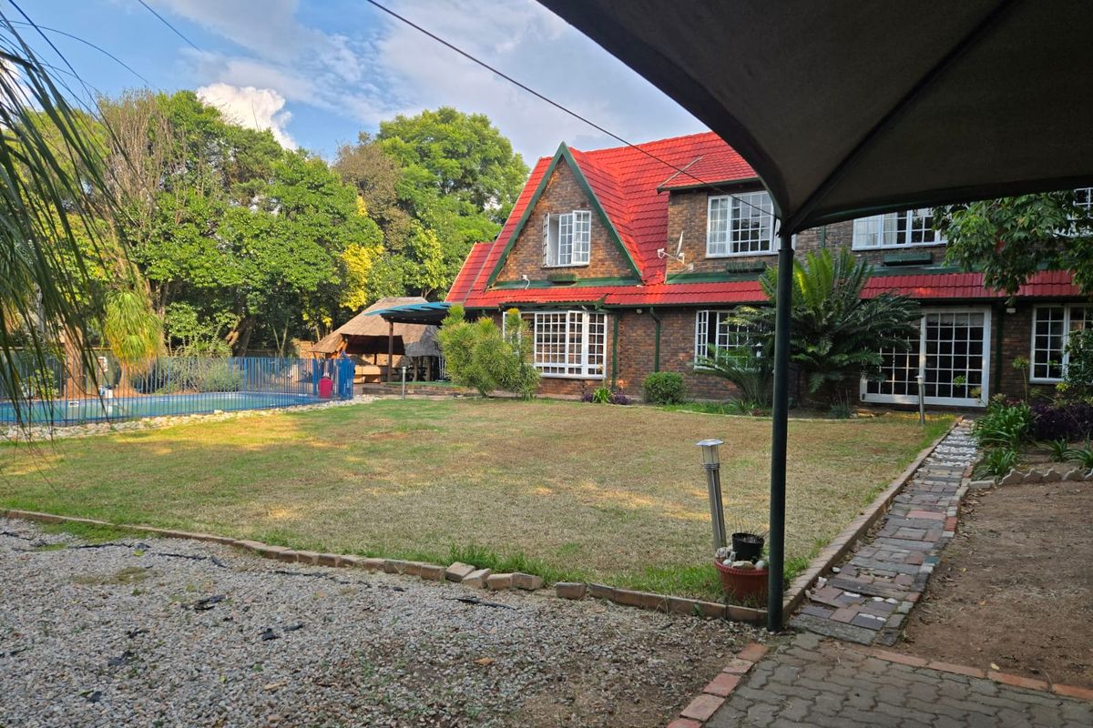 Spacious rear garden featuring a brick-faced home with a red tiled roof, swimming pool, and a detached thatched lapa area.