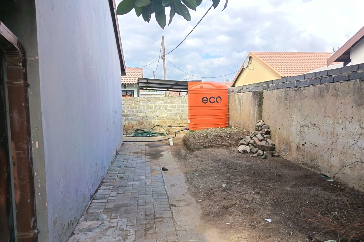 Rear exterior area featuring a water storage tank, paved walkway, and boundary walling, requiring maintenance and landscaping improvements.
