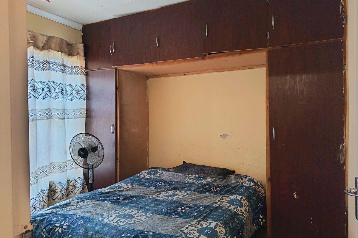 Bedroom featuring dark wood built-in cupboards with overhead storage units and visible wall surface wear.