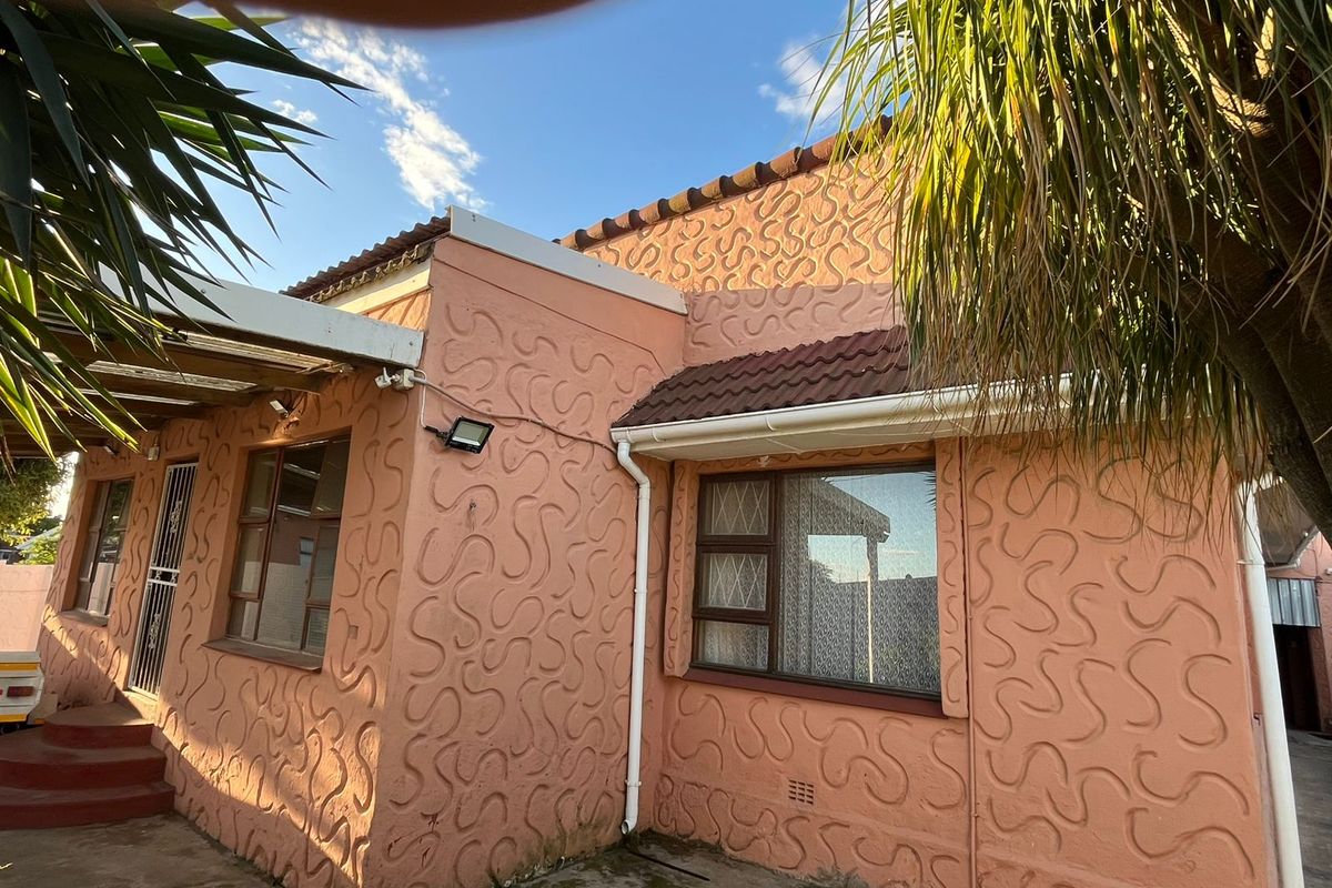 Rear exterior view of the house featuring a unique textured stucco facade, tiled roof, and security gate access.