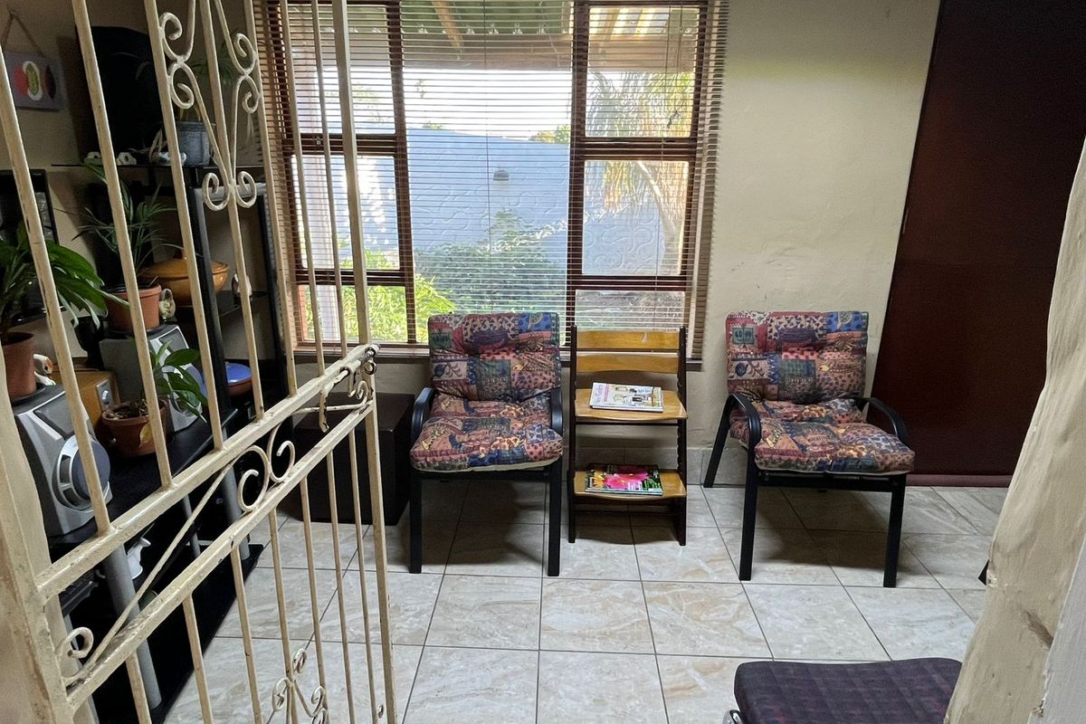 A living area featuring tiled flooring, venetian blinds, and a decorative security gate, providing a functional space with potential for cosmetic updates.