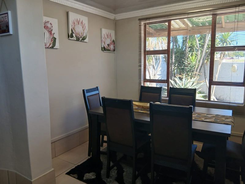 A dining room featuring tiled flooring, crown molding, and a large window with venetian blinds overlooking the garden.
