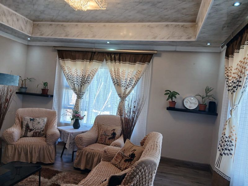 A cozy living room featuring a decorative tray ceiling with recessed lighting, laminate flooring, and built-in floating shelves.