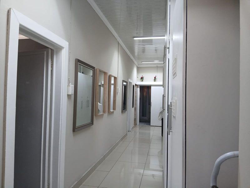 A clean, well-lit hallway featuring tiled flooring, neutral wall finishes, and built-in storage cupboards providing access to various rooms.