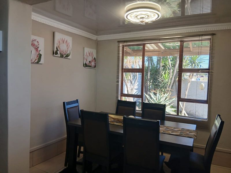 A dining room featuring a glossy ceiling, decorative crown molding, and a large window with venetian blinds overlooking the garden.