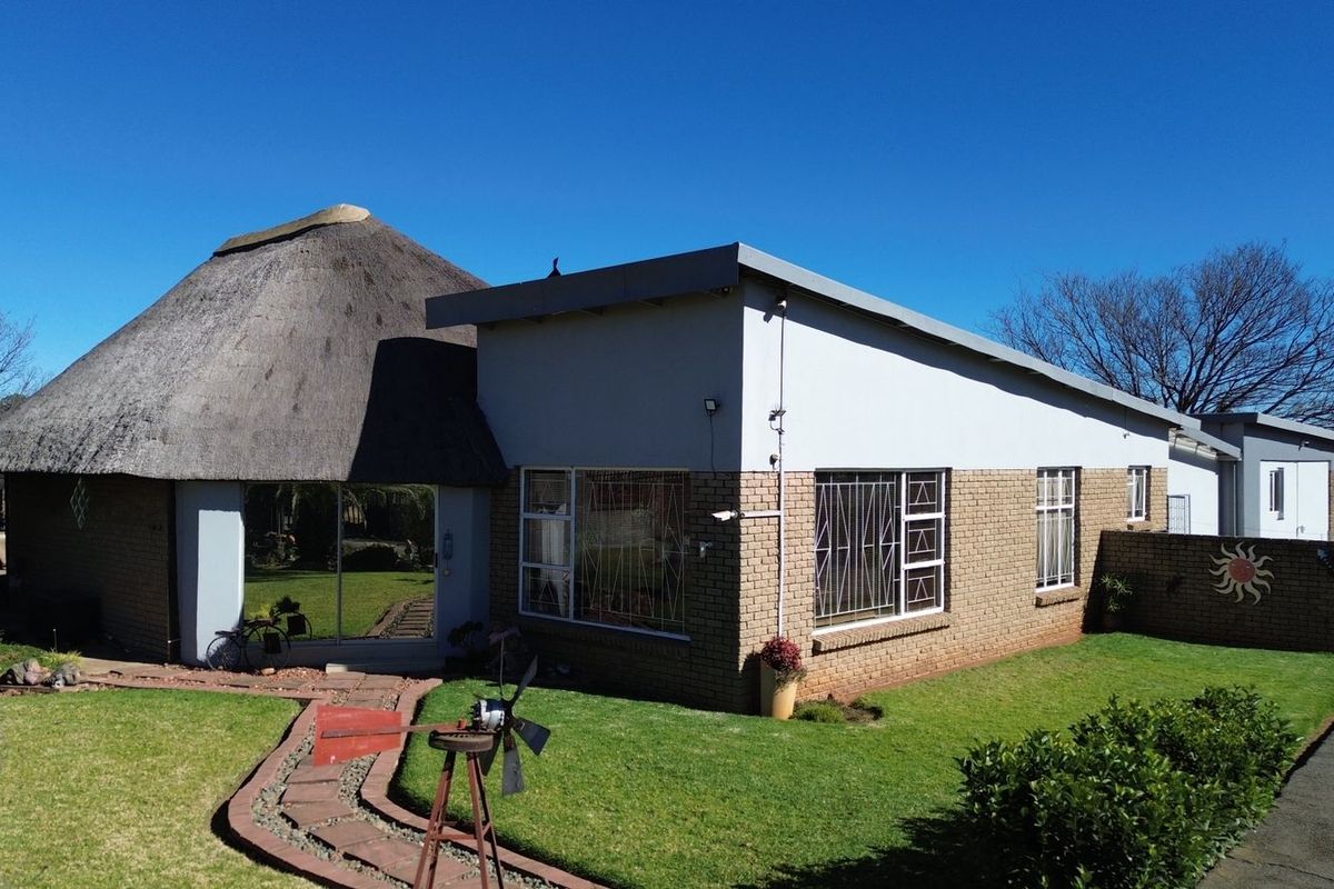 Rear view of a small holding property featuring a combination of thatched and modern brick architecture with a well-maintained garden and paved walkway.