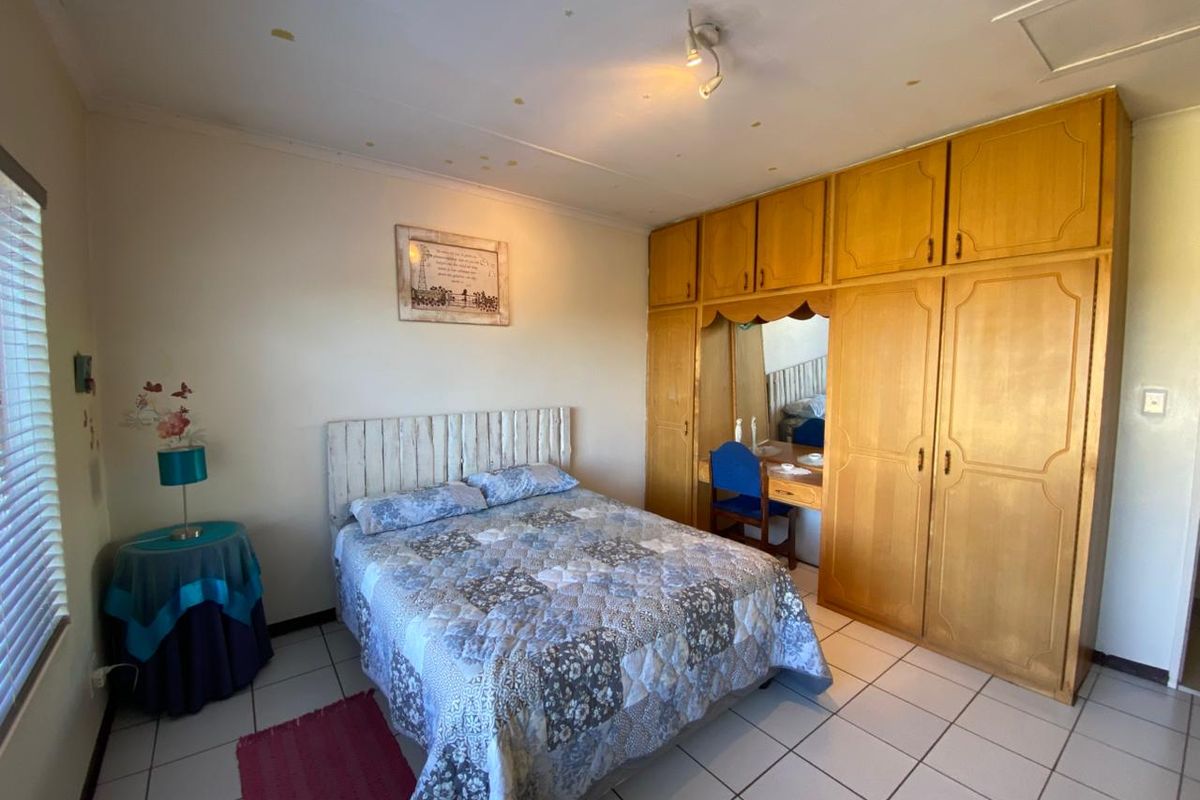 A bedroom featuring built-in wooden cupboards with an integrated vanity, tiled flooring, and window blinds.
