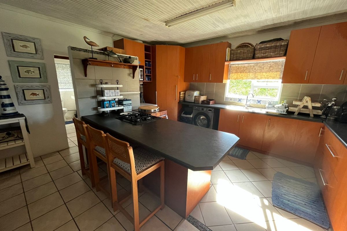 A functional kitchen featuring wood-finish cabinetry, a central island with a gas hob, tiled flooring, and direct access to an adjacent bathroom area.