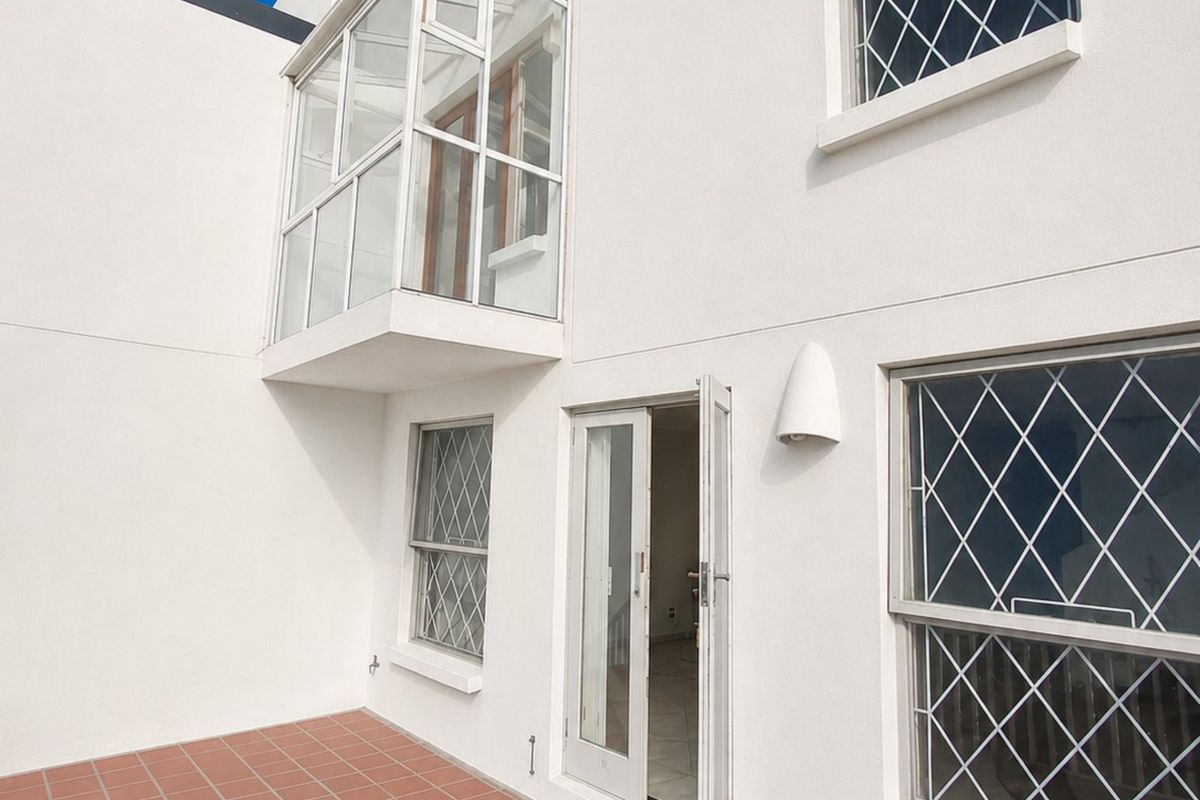 Rear exterior view of the townhouse featuring a terracotta tiled patio, enclosed balcony, and windows fitted with diamond-pattern security bars.