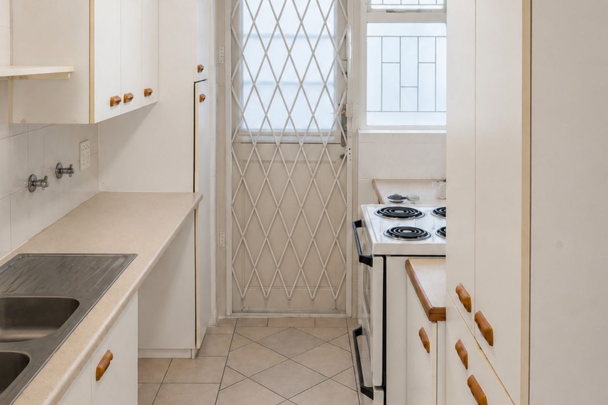 Functional galley-style kitchen featuring laminate countertops, built-in cabinetry, stainless steel sink, and direct access to the exterior via a security gate.