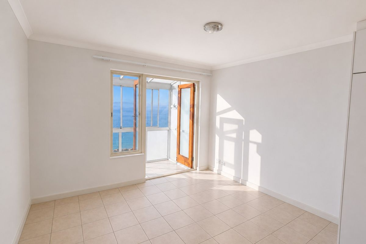 Bright and spacious bedroom featuring neutral tiled flooring, built-in storage, and direct access to a private balcony with scenic ocean views.