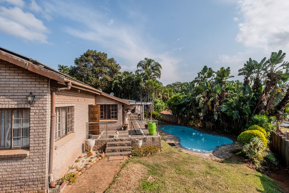 Rear view of the property featuring a brick facade, a paved patio area, and a swimming pool set within a landscaped garden.