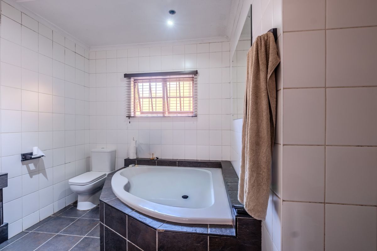 A functional bathroom featuring a built-in corner bathtub, toilet, and neutral tiled finishes throughout.