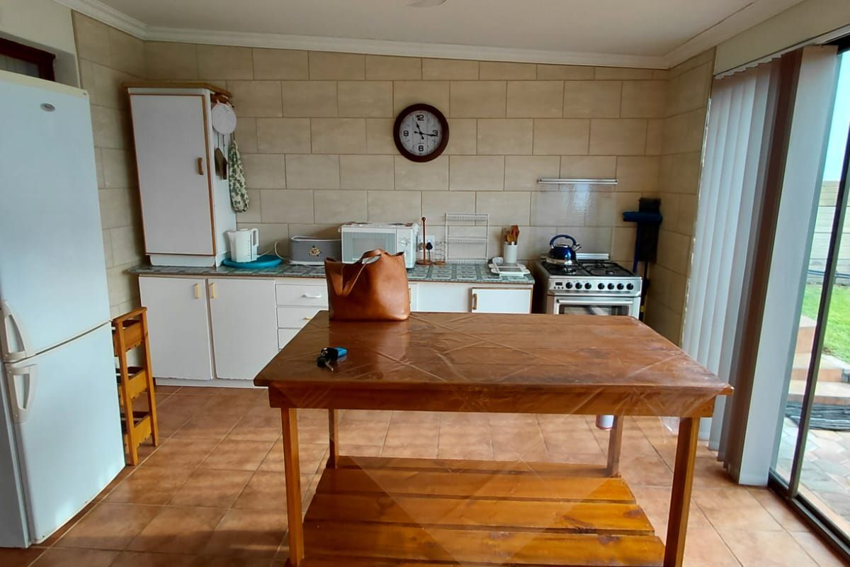 A functional kitchen featuring tiled flooring, a tiled splashback, built-in cabinetry, and a freestanding stove, with direct access to an outdoor area via sliding doors.