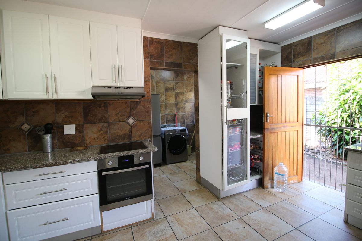 Functional kitchen featuring white cabinetry, granite countertops, built-in oven and hob, with an adjacent scullery area and direct access to the exterior.