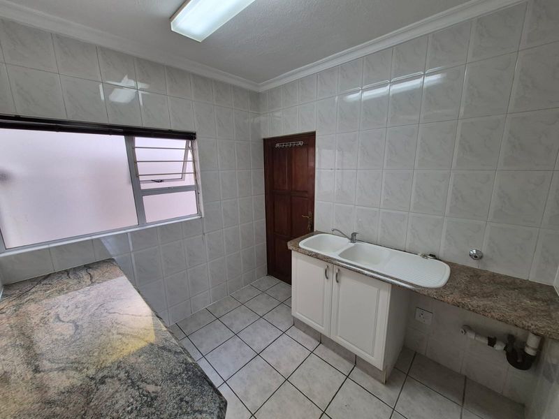 A functional scullery featuring tiled walls, granite countertops, a double basin sink, and dedicated plumbing connections for laundry or kitchen utility use.