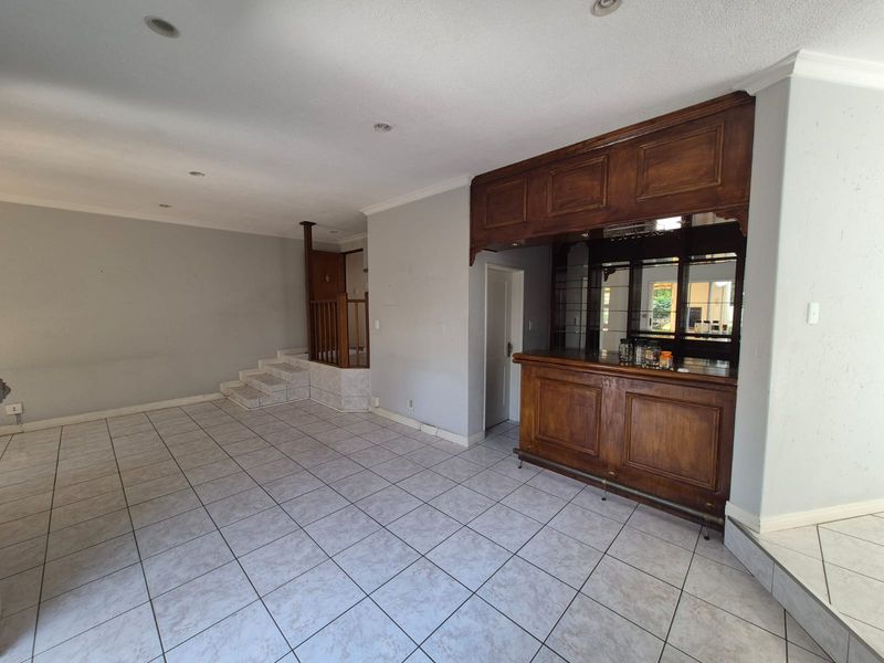 Spacious living area featuring a built-in wooden bar with overhead cabinetry, mirrored backing, tiled flooring, and an adjacent staircase with a wooden balustrade.