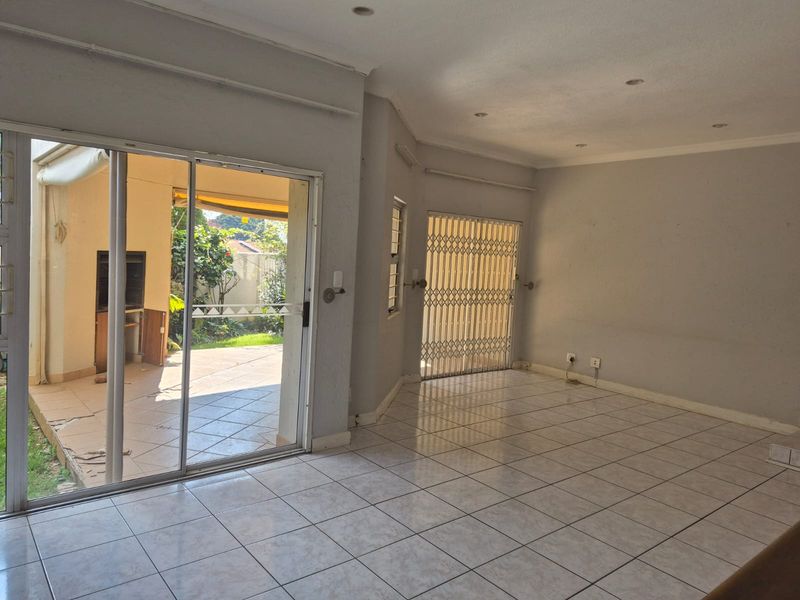 Spacious, tiled living area featuring large sliding doors leading to an outdoor patio, providing natural light and direct access to the garden.