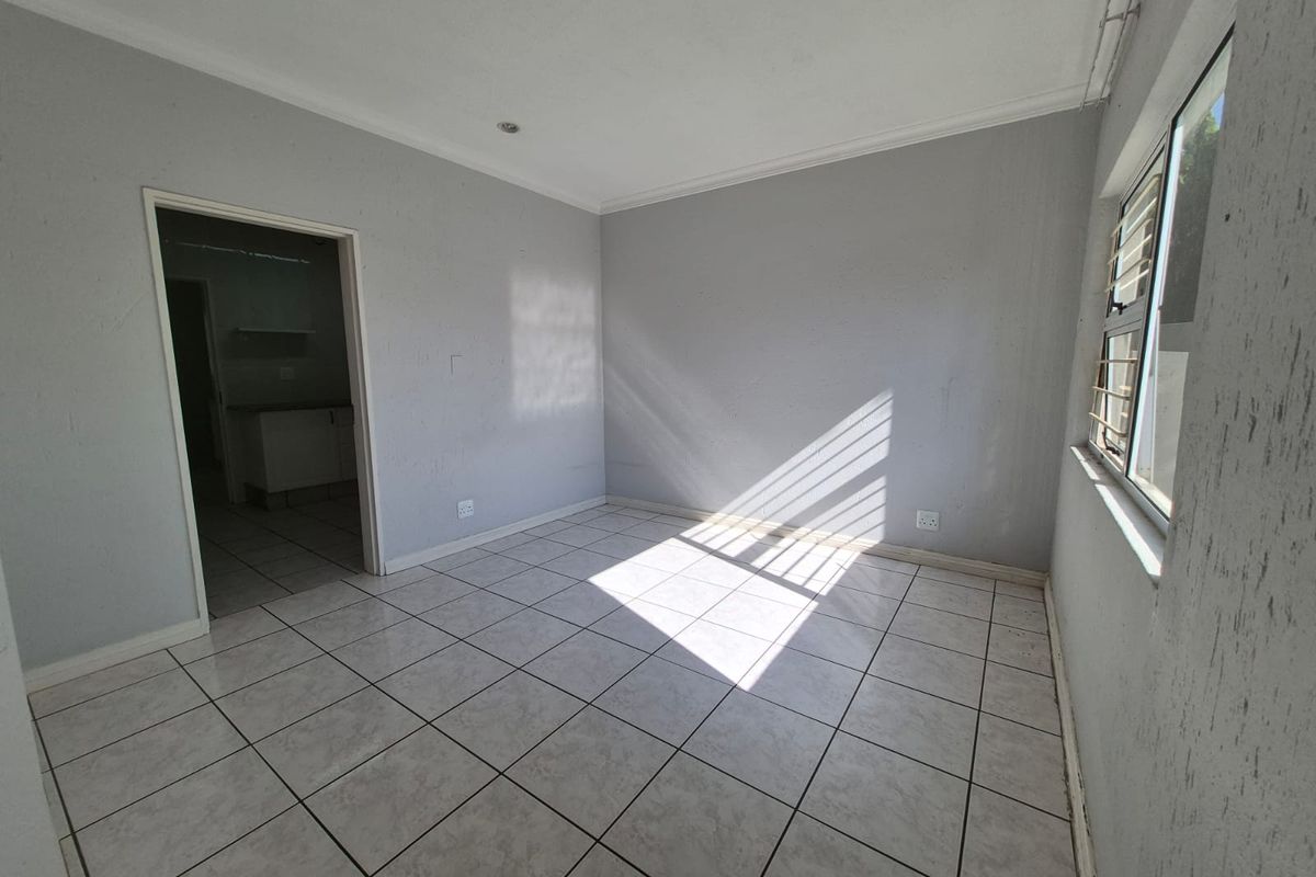 An empty living room featuring neutral tiled flooring, recessed downlights, and natural light streaming through windows with security bars.