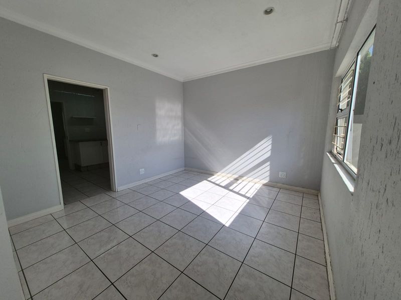 An empty living room featuring neutral tiled flooring, recessed downlights, and natural light streaming through windows with security bars.