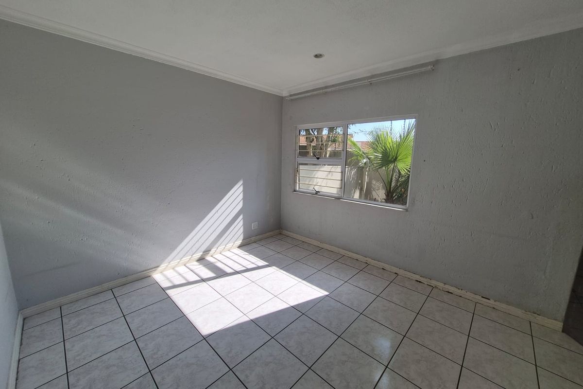 An empty bedroom featuring tiled flooring and a window with an aluminium frame, requiring minor finishing touches like skirting boards.