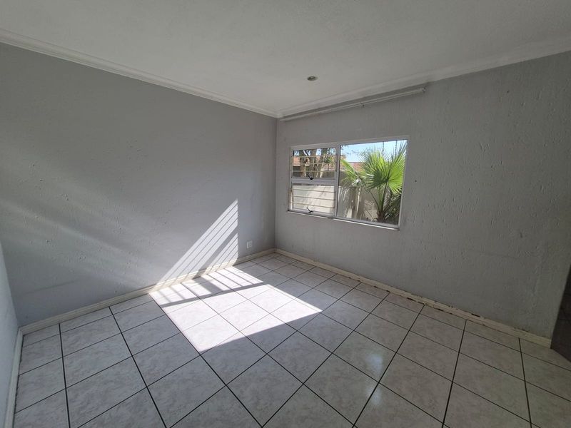 An empty bedroom featuring tiled flooring and a window with an aluminium frame, requiring minor finishing touches like skirting boards.
