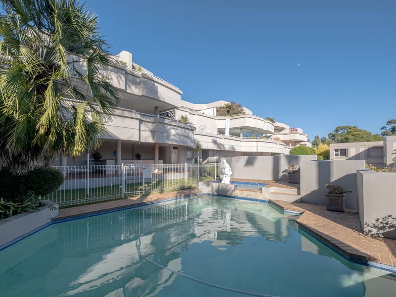 A communal swimming pool area featuring a water feature, brick coping, and views of the multi-level townhouse complex balconies.