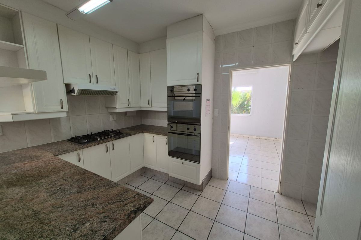 A functional kitchen featuring built-in cabinetry, granite countertops, a gas hob, and a double oven, with tiled flooring and direct access to an adjacent room.