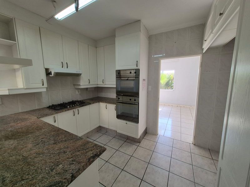A functional kitchen featuring built-in cabinetry, granite countertops, a gas hob, and a double oven, with tiled flooring and direct access to an adjacent room.