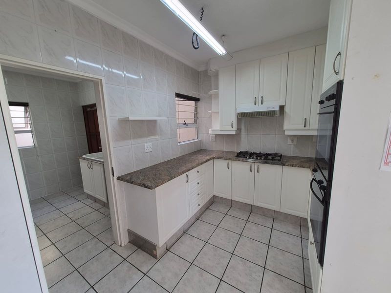 A functional kitchen featuring white cabinetry, granite countertops, built-in oven, gas hob, and tiled finishes, with an adjacent scullery area.