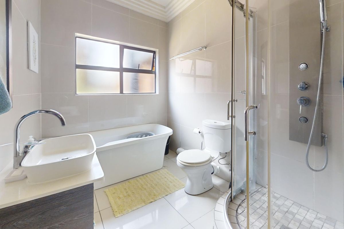 Modern bathroom featuring a freestanding bathtub, separate shower enclosure with body jets, vessel sink vanity, and neutral floor-to-ceiling tiling.