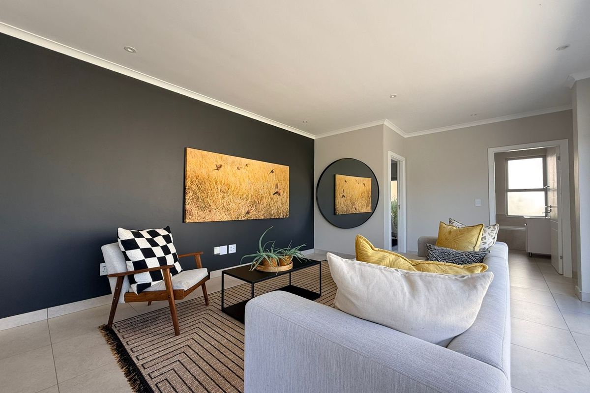 A modern, well-maintained living room featuring a striking dark accent wall, neutral tiled flooring, and recessed downlighting.