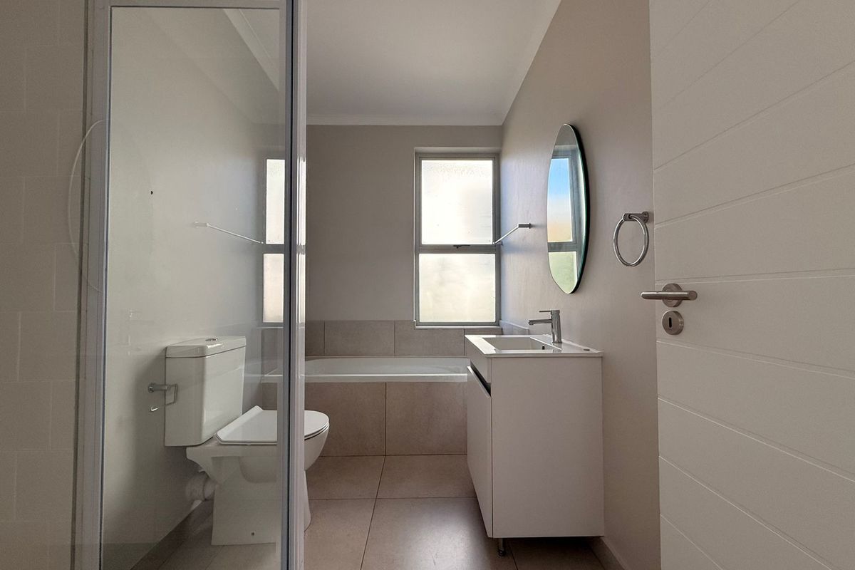 A clean, modern bathroom featuring a shower enclosure, bathtub, vanity cabinet with basin, and neutral tiled finishes throughout.