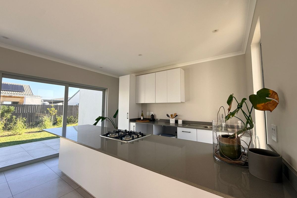 Modern kitchen featuring a central island with a gas cooktop, stone countertops, sleek cabinetry, and large sliding doors opening to the garden.