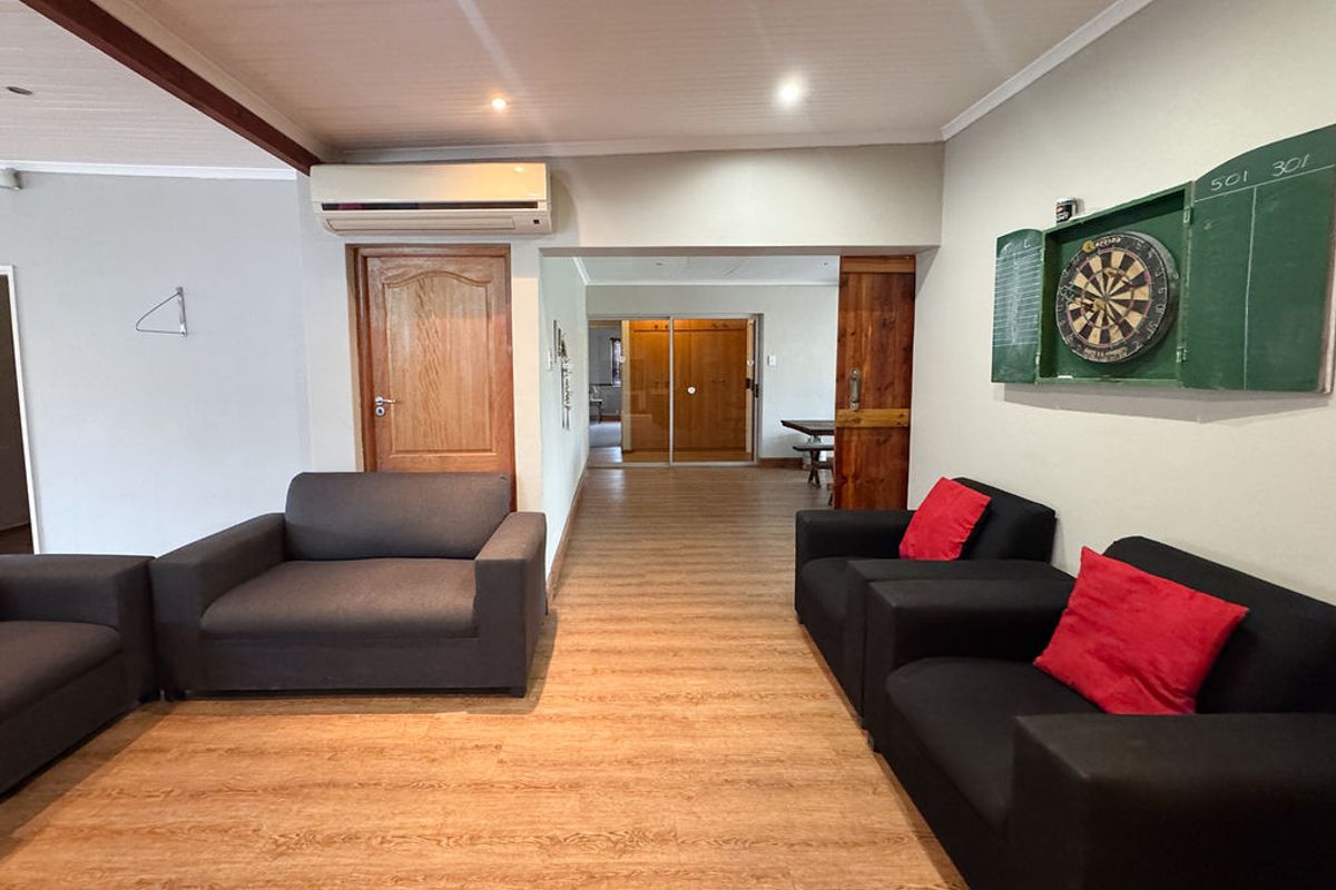 A spacious living area featuring wood-look laminate flooring, a wall-mounted air conditioning unit, and solid timber internal doors.