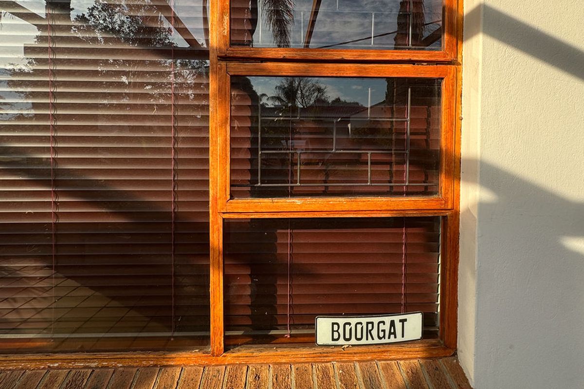 Exterior view of a timber-framed window with a brick sill, featuring integrated security bars and venetian blinds.