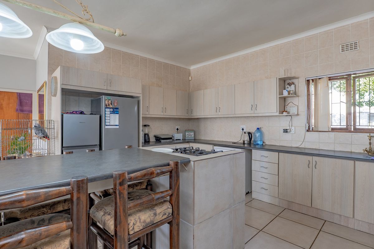A functional kitchen featuring light-toned cabinetry, a central island with a gas hob, tiled backsplash, and tiled flooring.